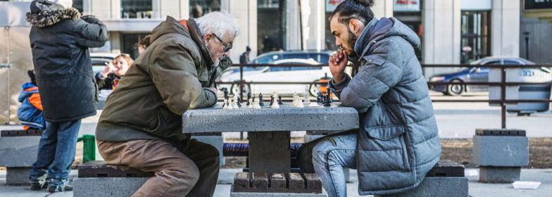 Une jeune personne et une personne plus âgée jouent aux échecs sur une table publique