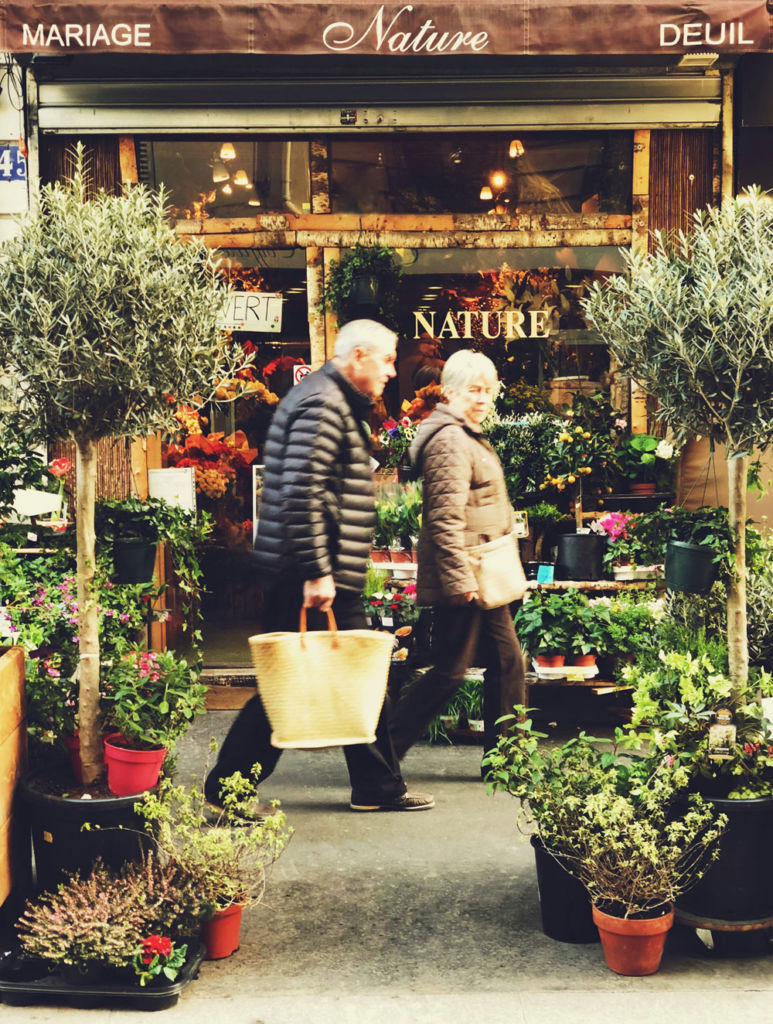 Deux personnes âgées dans la rue passant devant un fleuriste