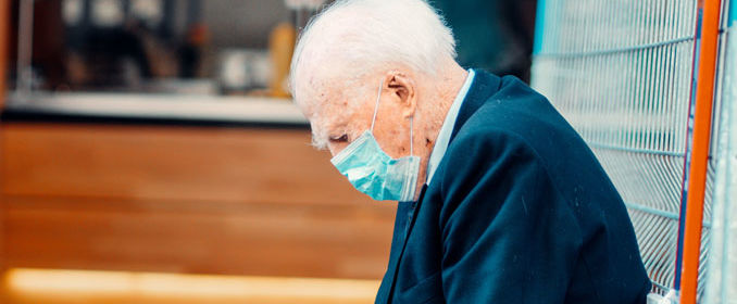 Une personne âgée portant le masque appuyée sur un mur regardant le sol